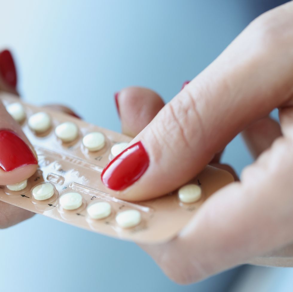 woman with red manicure holding contraceptive hormonal pills in her hands