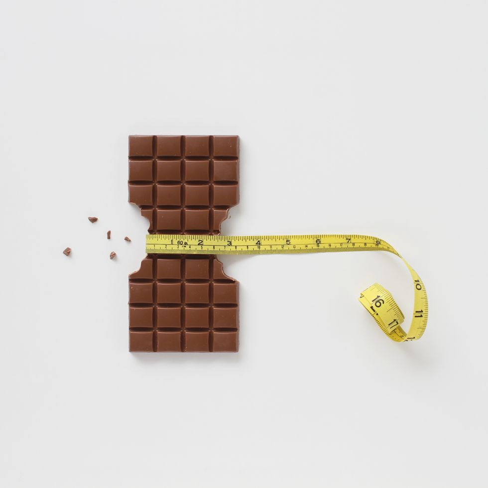 Block of chocolate bar with sides bitten off and chocolate crumbs with a tape measure around the middle