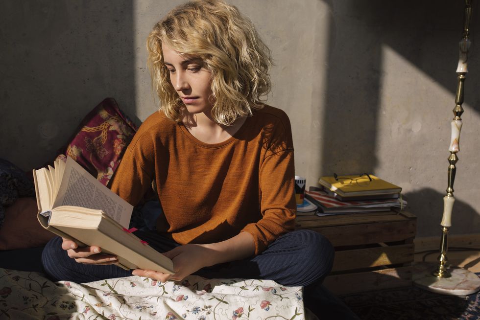 blond student sitting on bed reading a book
