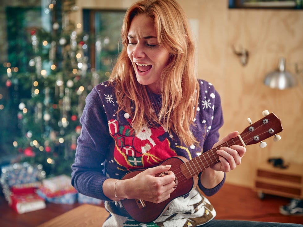blond woman playing ukulele in front of christmas tree
