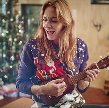 blond woman playing ukulele in front of christmas tree
