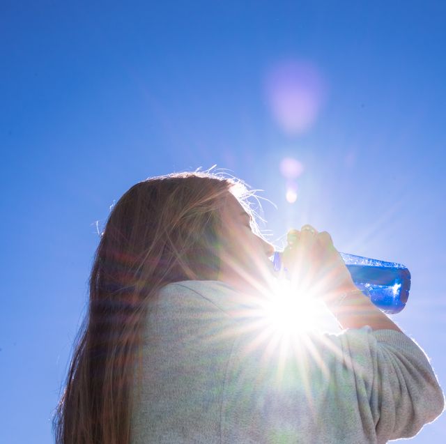 blonde woman drinking water outside while being illuminated by a ray of sunlight
