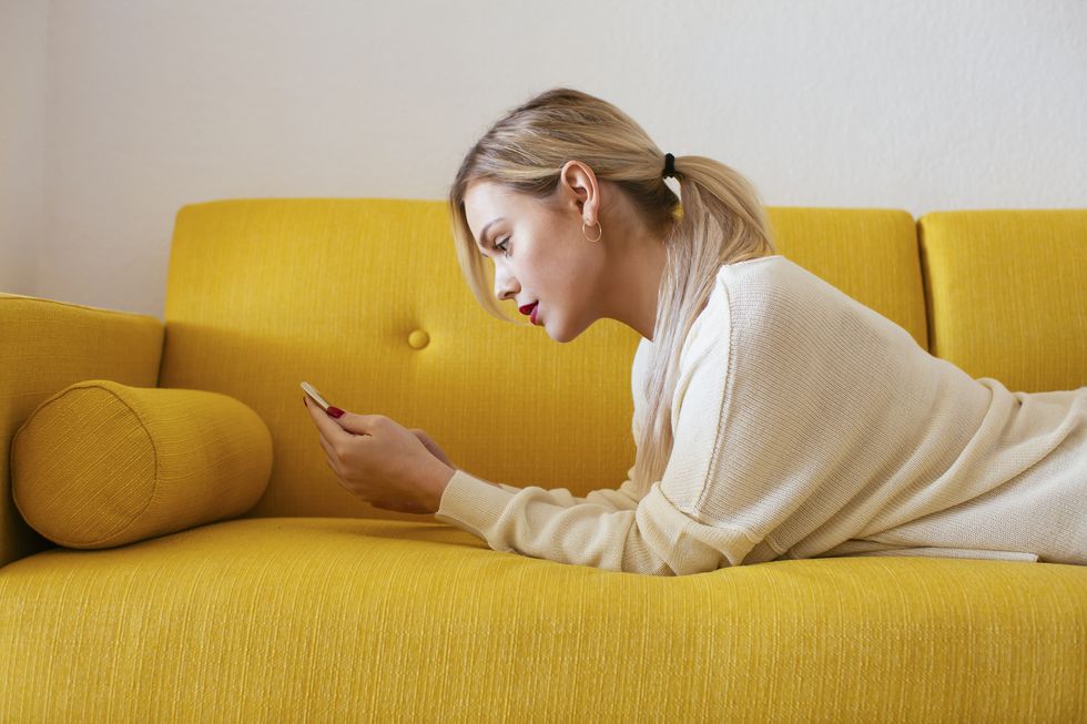 Blonde woman lying on sofa, using smartphone at home