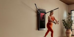 blonde woman in orange fitness outfit strength training with tonal home gym
