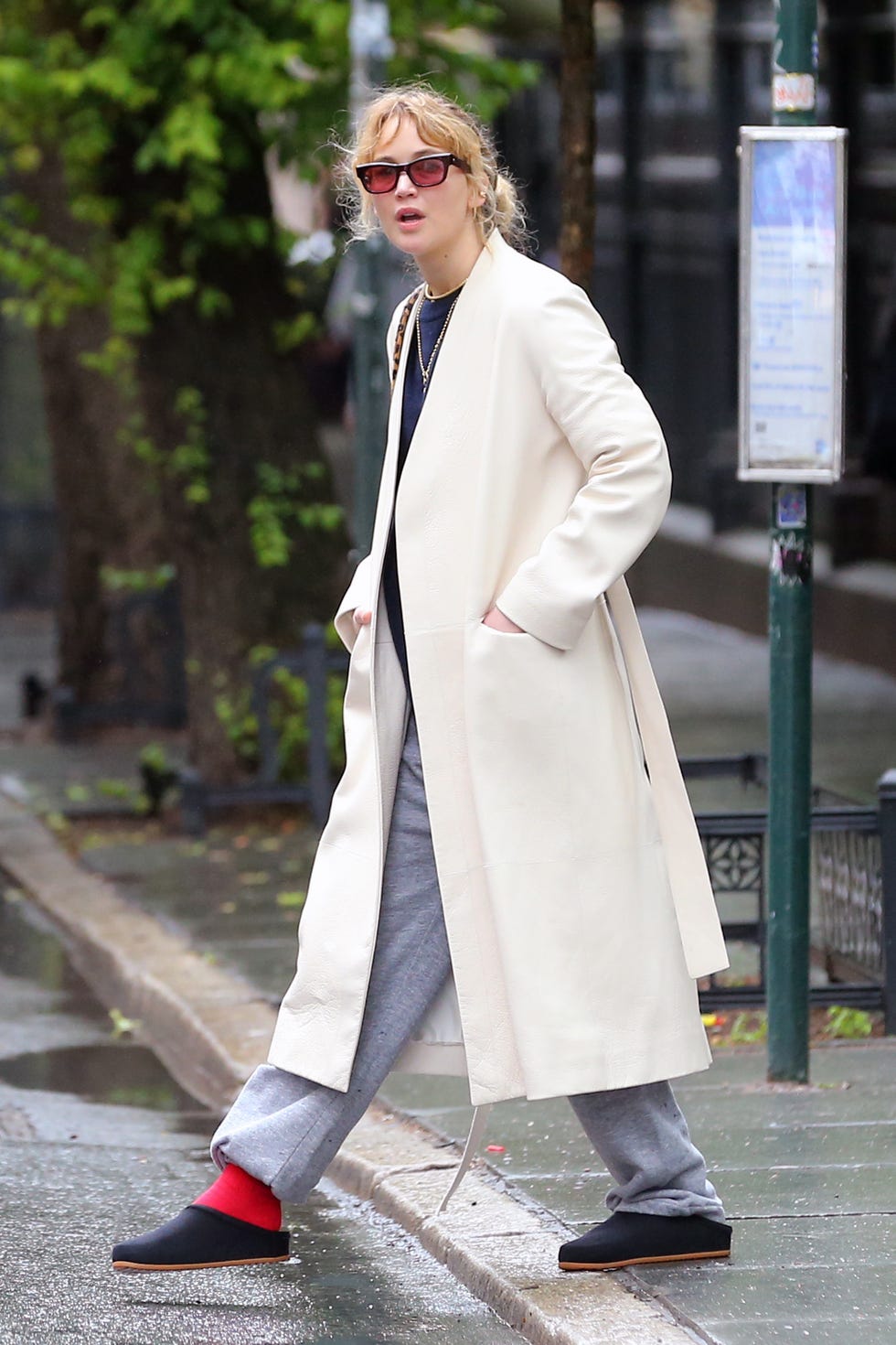 person walking on a wet sidewalk wearing a long coat and casual attire