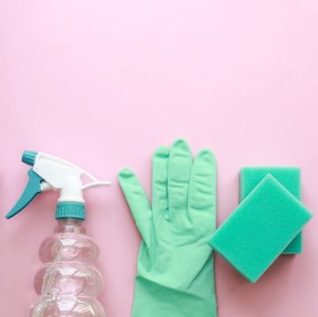 blue cleaning supplies bottle with chemicals, gloves, sponges and brushes over pink background flat lay with copy space