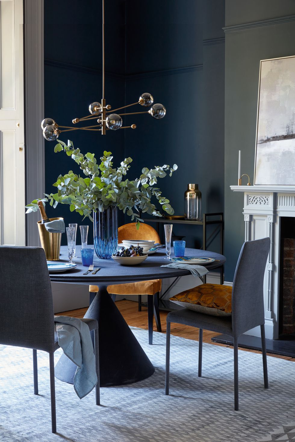 dining room round dining table, blue vase in the middle of the tablerich palettefor a luxurious look, use the same shade on walls and furniture an accent chair in velvet and polishedbrass accessories add layers of interest in this elegant schemewalls in velvet blue elite emulsion, £4625l, zoffany clay table, £5,845 by desalto bronte chairs in indigo velvet, £399 for two all heal’s manipur ochre cushion, £75, designers guild moritz chair in amber, £299, john lewis  partners lena brass champagne cooler, £72 elsa fluted champagne glasses, £32 for two all rowen  wren bubble glasses in deep blue, £11 each, by memento, the conran shop ripple column vase, £69, heal’s kelp bowls, £38 each, by brickett davda slate linen napkins, £1250 each all the conran shop constantine bay dinner plates, £14 each, by rick stein at unique  unity jenny salad plates, £28 each, 1882 ltd matt gold 16 piece cutlery set, £75 abstract skyline framed canvas, £195 both cox  cox pendant light, £180, debenhams katiya platinum rug, £1,195, designers guild