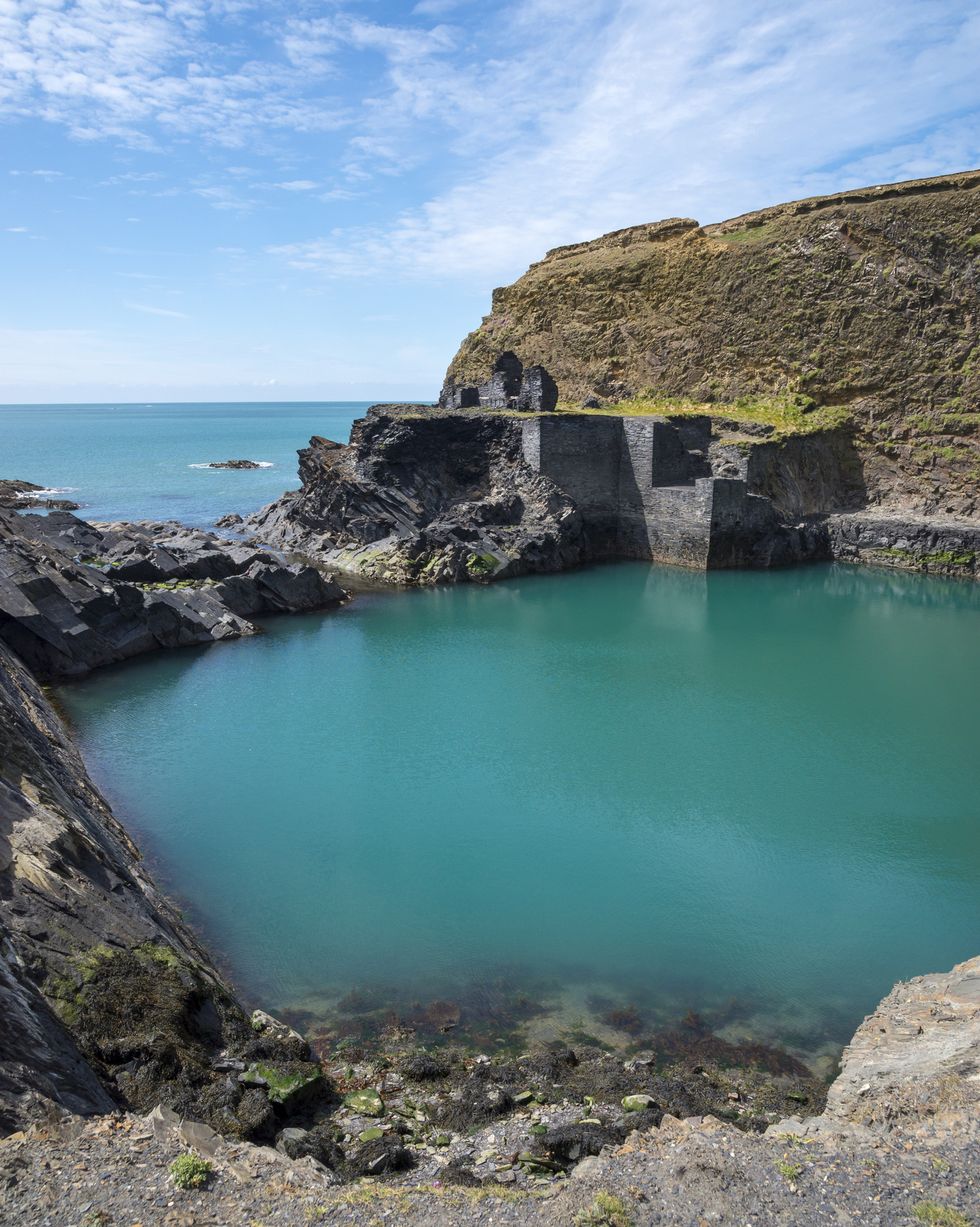 well known feature in the pembrokeshire coast national park an old quarry flooded by the sea to create a deep blue pool remains of the old buildings by the water