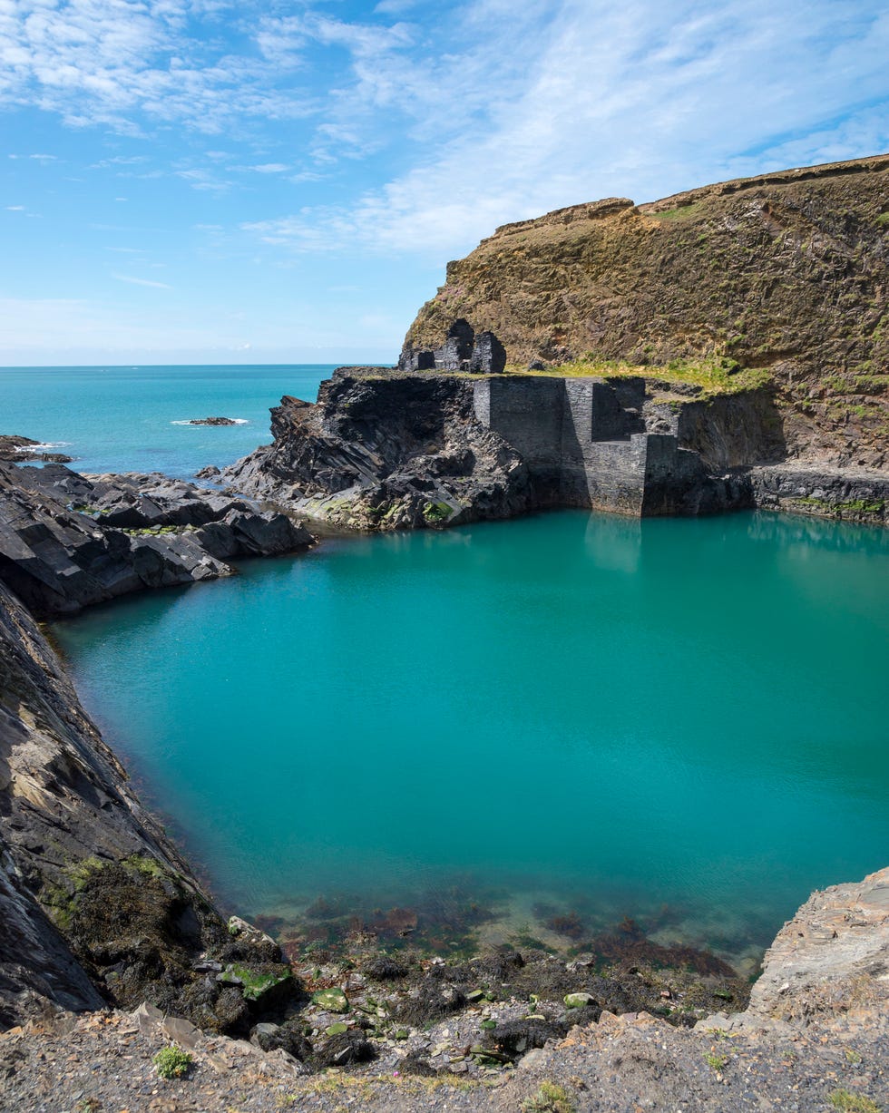 well known feature in the pembrokeshire coast national park an old quarry flooded by the sea to create a deep blue pool remains of the old buildings by the water