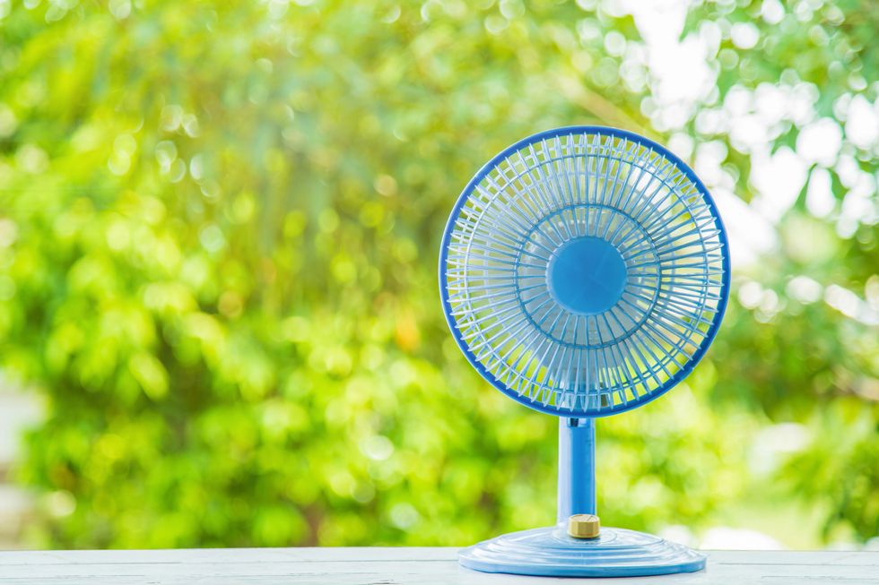 a blue plastic desktop electric fan on white wooden table with green blurred nature background