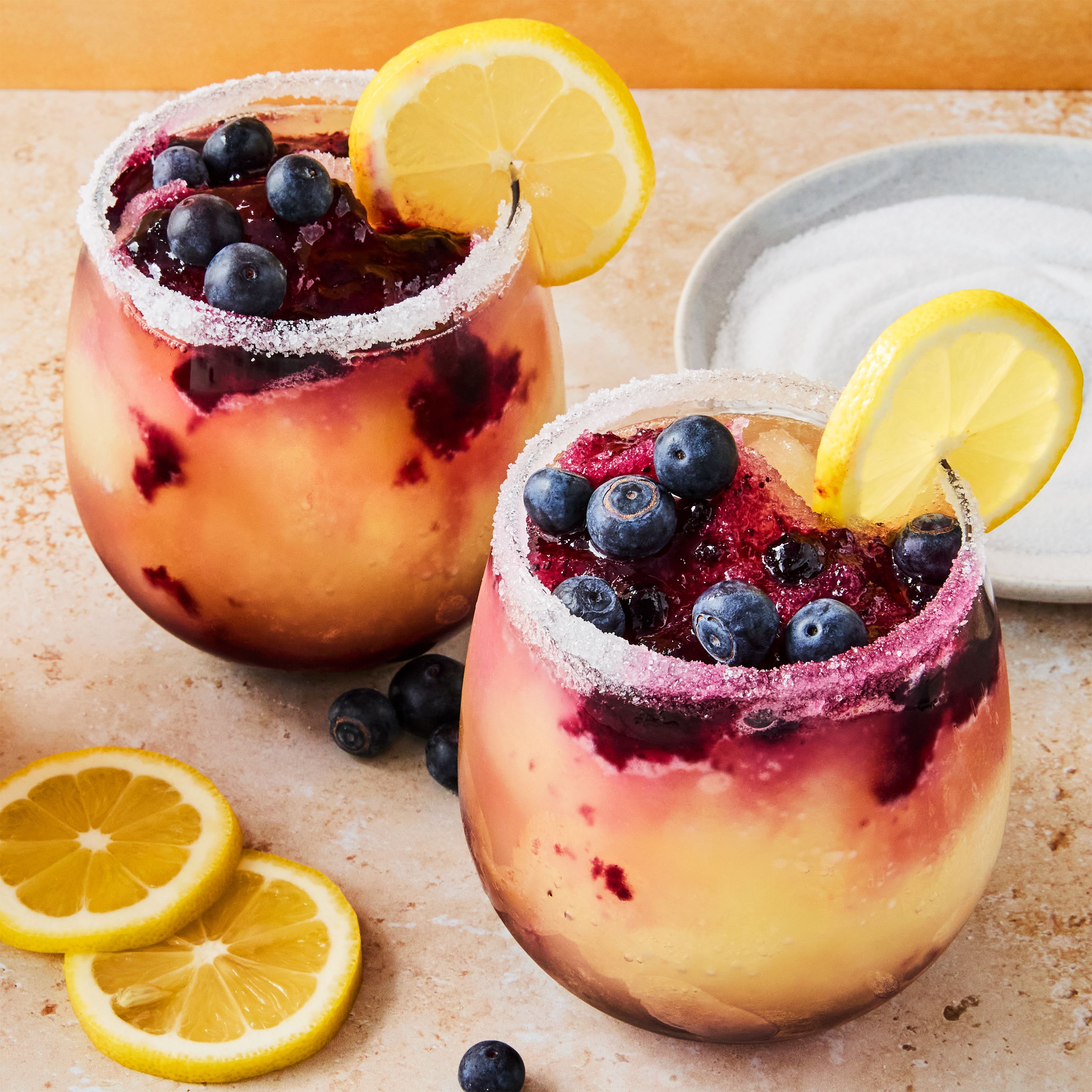 Frozen blueberry lemon cocktails in stemless glasses with sugared rims and fresh garnishes