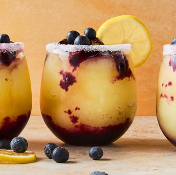 Frozen Blueberry Lemon Drop Slushies stemless glasses filled with a frozen vodka lemon cocktail with a blueberry syrup swirled in the glass. garnished with a sugared rim, lemon wheels, and fresh blueberries