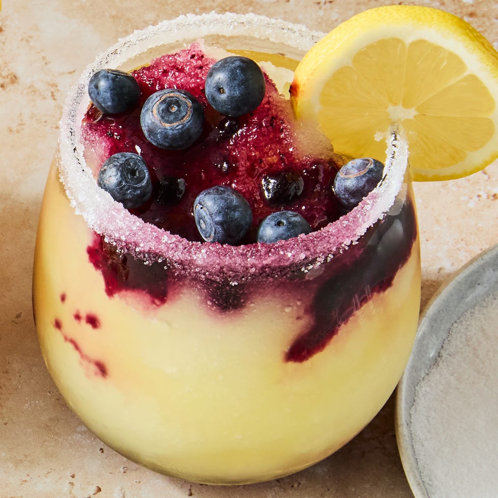 stemless glasses filled with a frozen vodka lemon cocktail with a blueberry syrup swirled in the glass. garnished with a sugared rim, lemon wheels, and fresh blueberries