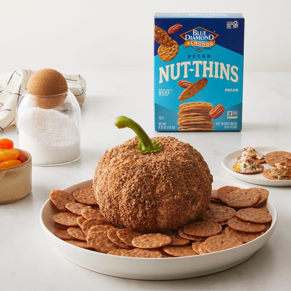 a festive snack arrangement featuring a cheese ball shaped like a pumpkin surrounded by crackers and a box of nut thins