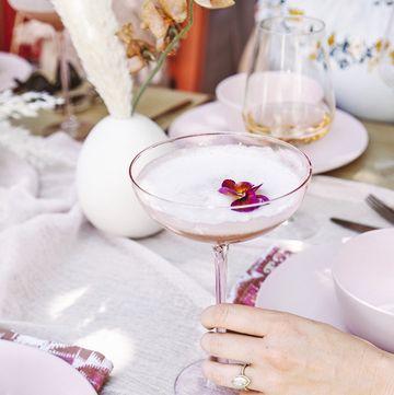 blushing pisco sour in a wide stemmed glass being held by a hand