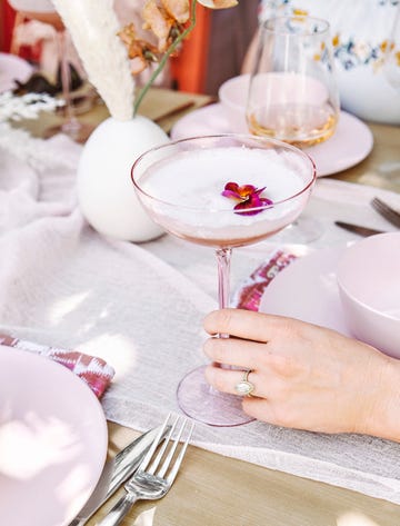 blushing pisco sour in a wide stemmed glass being held by a hand