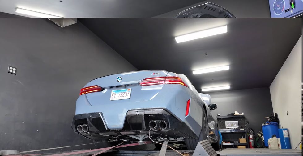 Rear view of a blue BMW M3 being tested on a dyno in a garage