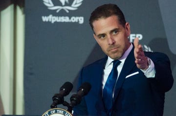 hunter biden wearing a blue suit and tie, gesturing forward with his left hand while speaking into two microphones on a podium