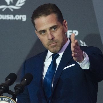 hunter biden wearing a blue suit and tie, gesturing forward with his left hand while speaking into two microphones on a podium