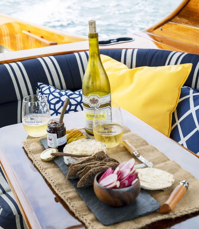 cheese, jam, crackers, crudités, and wine aboard a boat, yellow and blue pillows and cushions create a soft spot to sit
