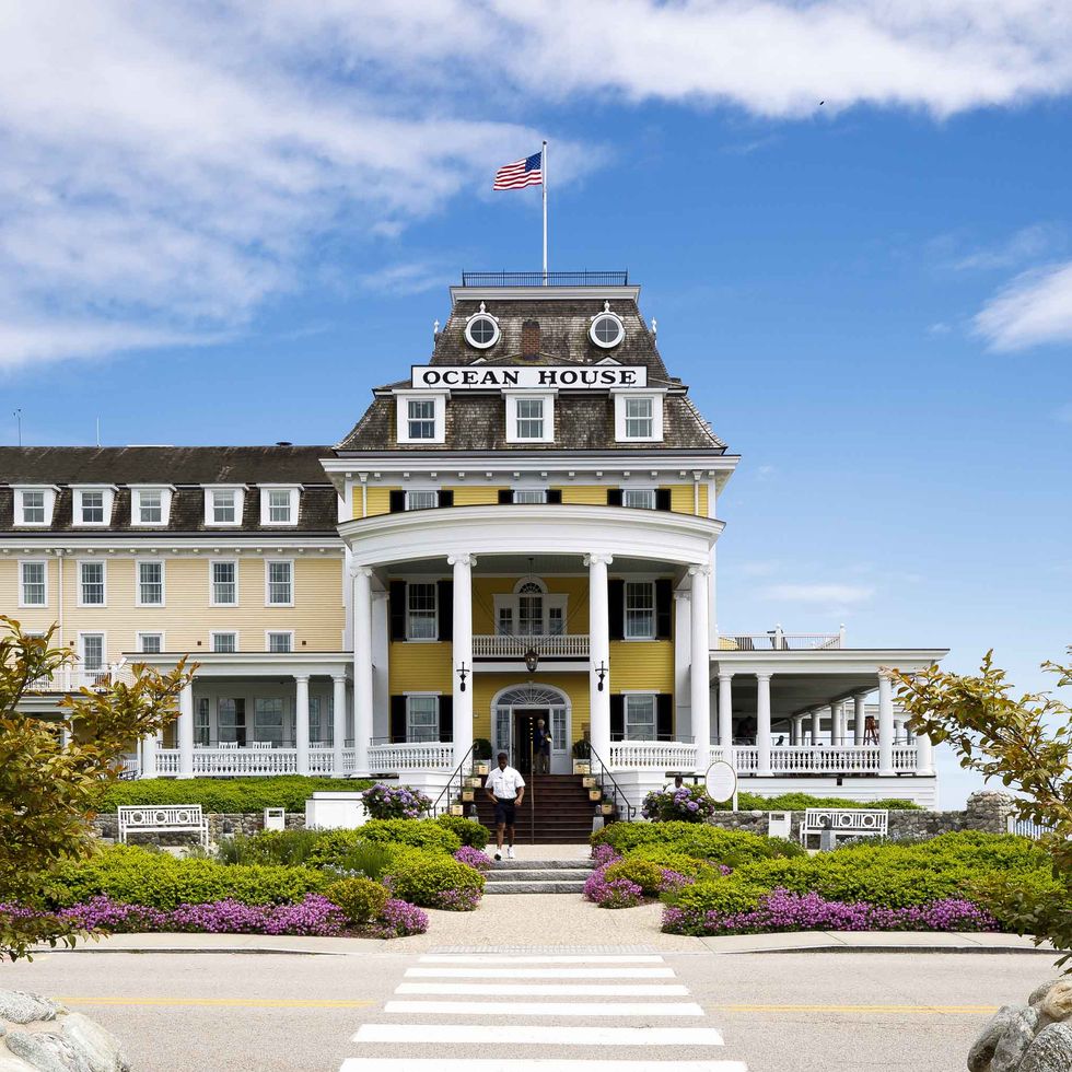 the entrance to the yellow and white ocean house inn, an american flag waves on the top