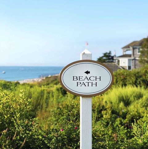 a white sign that says 'beach path' points to the beach and water a beach house is in the background