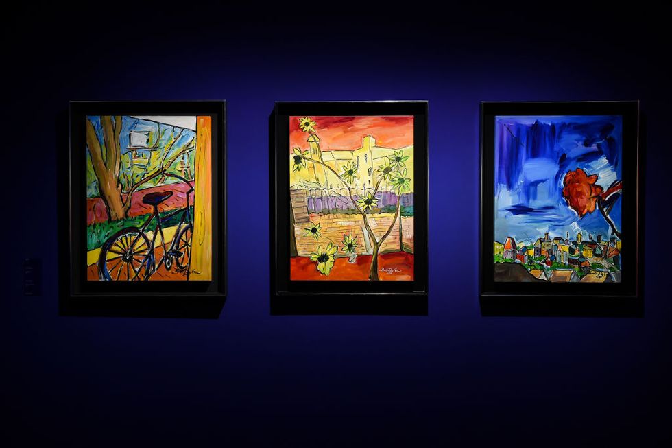 three color paintings hang from a dark blue wall, each painting is lit up