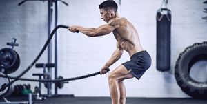 Gespierde man zonder shirt traint met battle ropes in de sportschool om vet kwijt te raken en spieren op te bouwen.