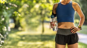 body part view of a good looking athlete holding a water bottle after running a half marathon during a warm summer sunset