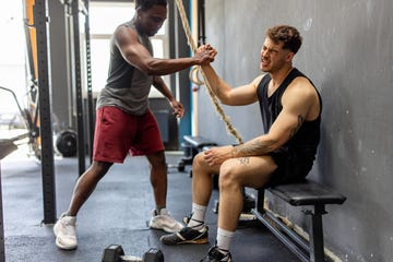 fitness man sitting on a bench giving a high five to his trainer, celebrating a successful dumbbell workout session in cross training gym