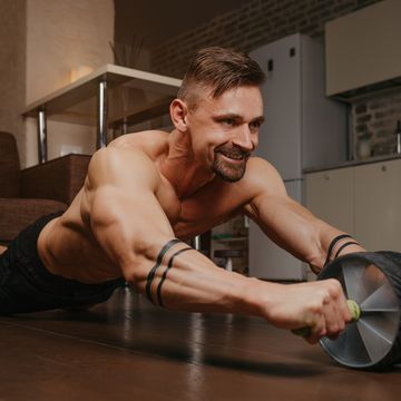 a bodybuilder with tattoos on his forearms is training with ab wheel at home