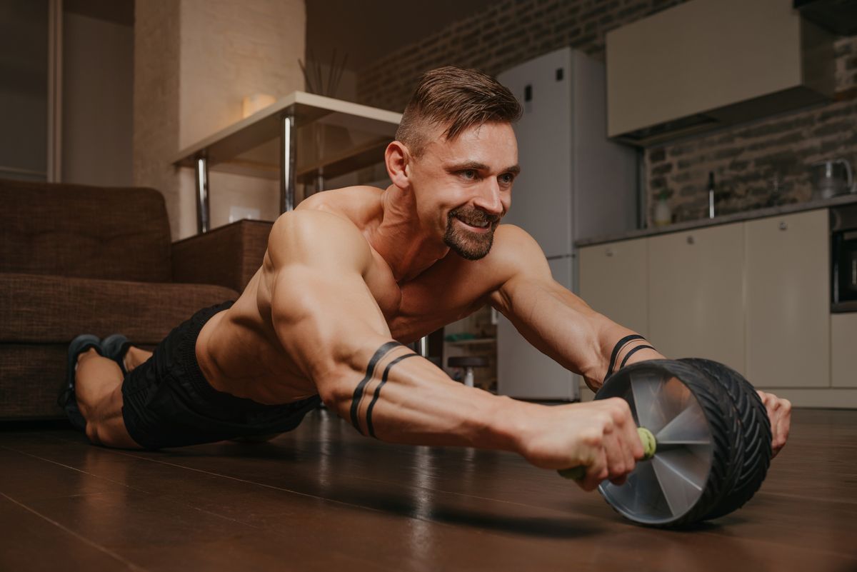 a bodybuilder with tattoos on his forearms is training with ab wheel at home