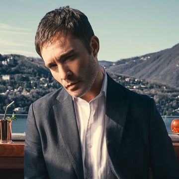 ed westwick wearing a grey suit in front of italian mountains