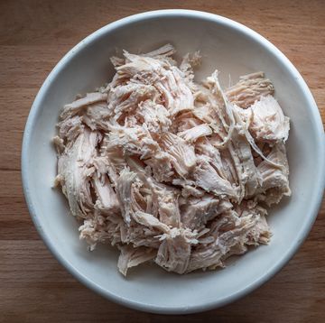 shredded chicken meat for salads in a deep plate stands on the kitchen board, top view close up