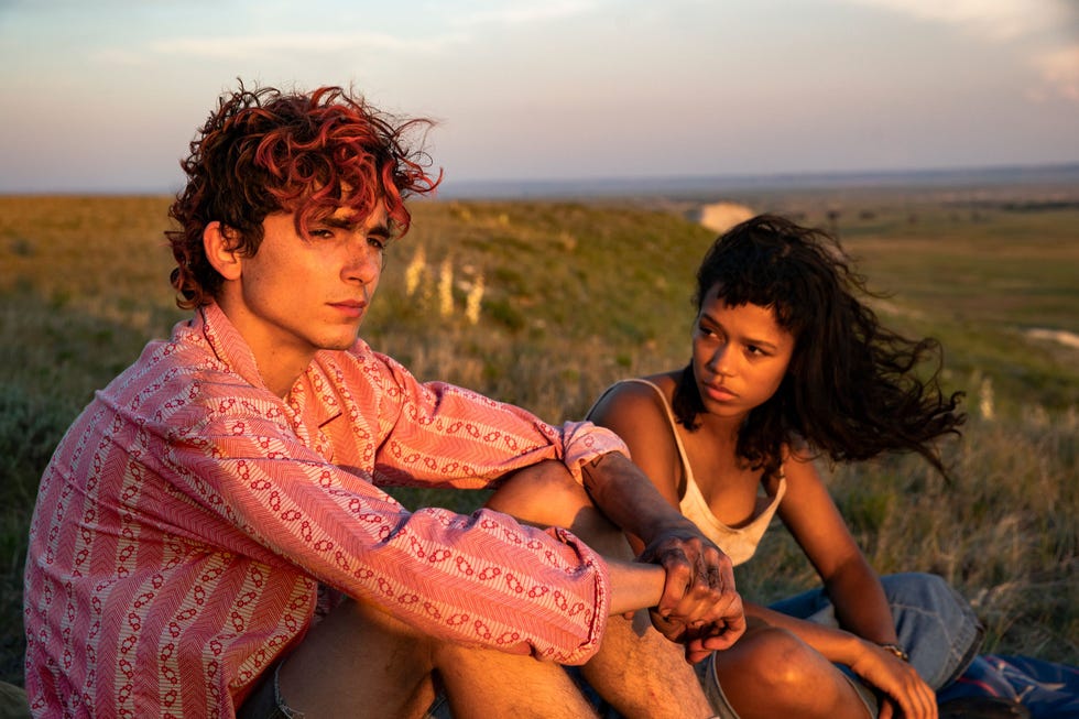 two individuals sitting close together on a grassy hill during sunset