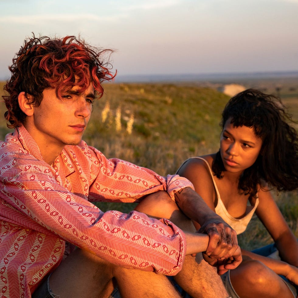 two individuals sitting close together on a grassy hill during sunset two individuals sitting close together on a grassy hill during sunset