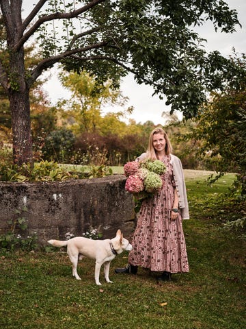 interior stylist and author mieke ten have posing in her upstate new york backyard with a large bouquet in hand and a dog by her feet