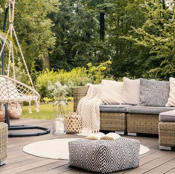 book on a black and white pouf in the middle of a bright terrace with a rattan corner sofa, hanging chair and round rug real photo