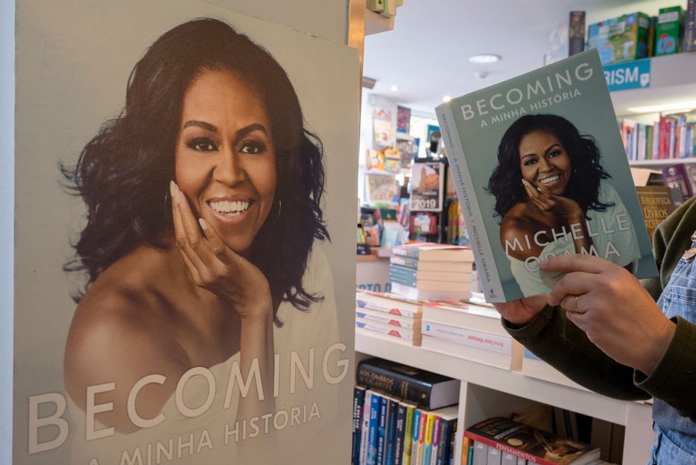a man holds open a copy of the michelle obama book becoming, in a bookstore, while standing next to a large cardboard image of the book cover