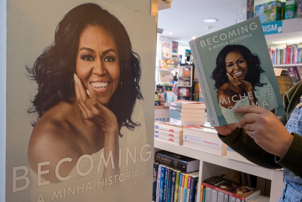 a man holds open a copy of the michelle obama book becoming, in a bookstore, while standing next to a large cardboard image of the book cover