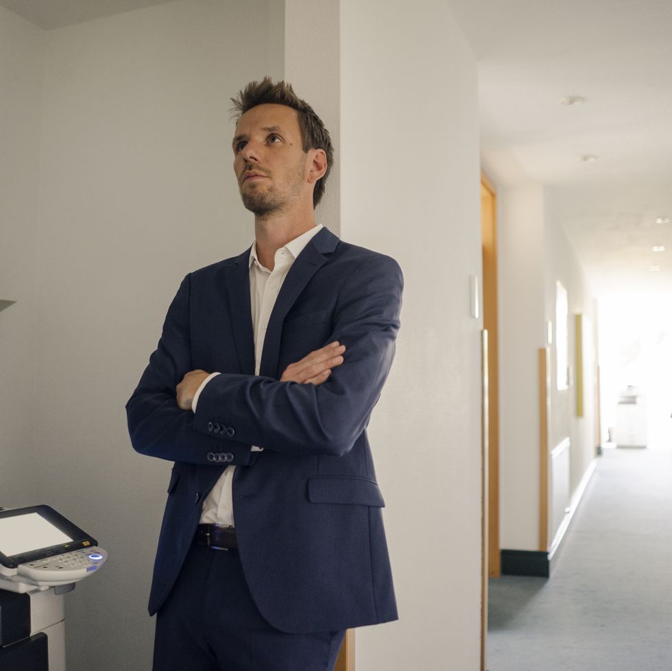 bored businessman leaning against wall next to copying machine