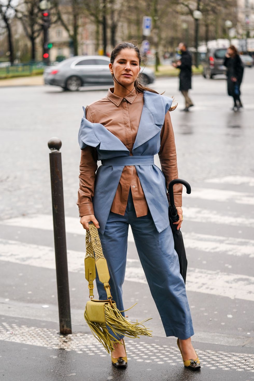 paris, france   february 27 a guest wears a brown leather shirt, a blue sleeveless jacket, blue pants, a yellow bag with fringes, pointy shoes, outside ann demeulemeester, during paris fashion week   womenswear fallwinter 20202021, on february 27, 2020 in paris, france photo by edward berthelotgetty images