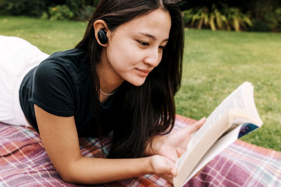 woman wearing bose quietcomfort wireless earbuds while reading