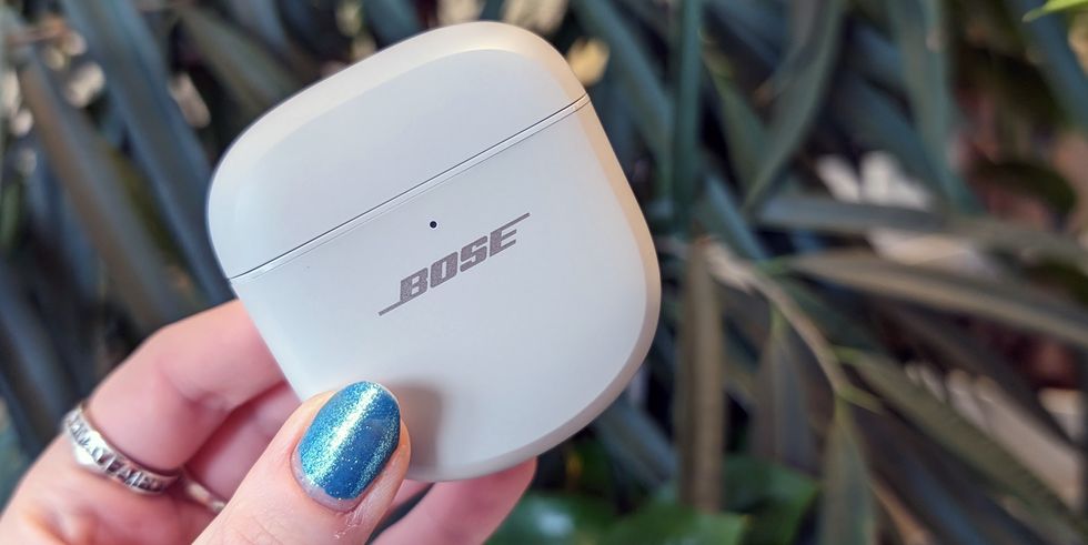 true wireless earbuds held up against green leaves by hand with blue nails