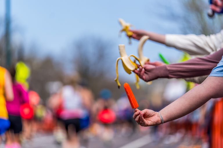 people hold out a popsicle and bananas for runners in a race