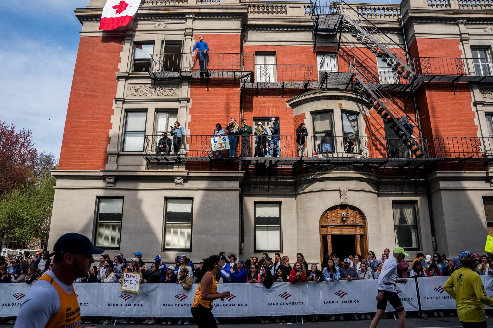 runners pass by a building in a race while spectators watch from the windows