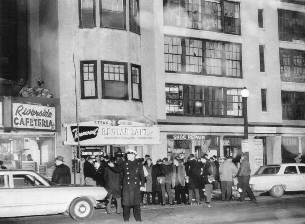 a crowd gathers in front of multistory apartment building, a police officer is standing in the street directing traffic in front of the crowd