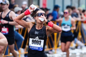 a participant in a marathon is seen in pouring water from a cup over their head wearing a sleeveless black top and has bright wristbands