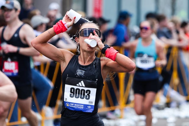 a participant in a marathon is seen in pouring water from a cup over their head wearing a sleeveless black top and has bright wristbands