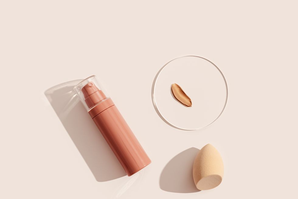 bottle of makeup foundation cream, samples on glass disk, beauty blender sponge on beige color background with hard light skin care beauty product top view package concealer base container
